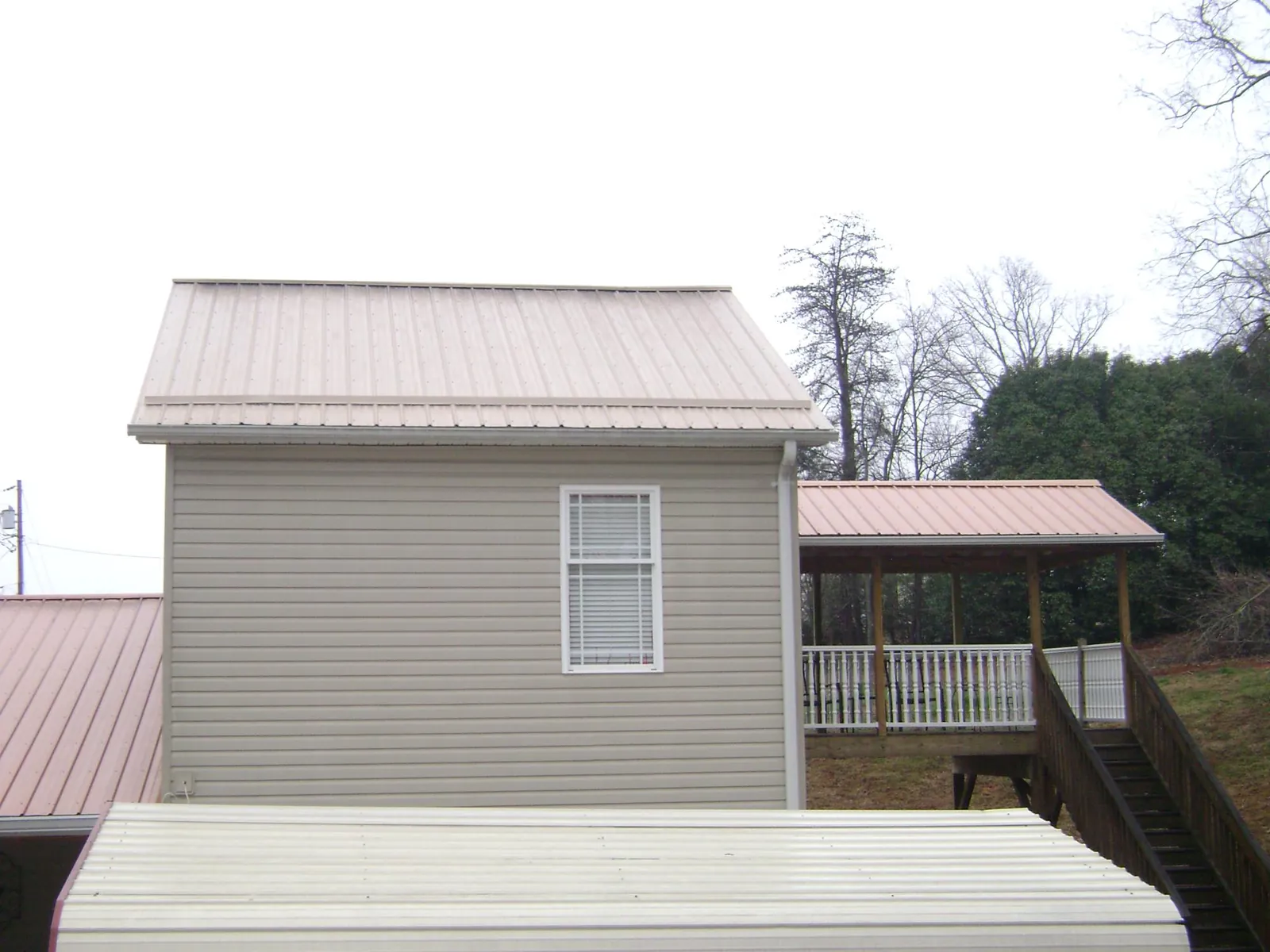 Tan metal roofs on a two story addition and attached porch, from a Roof Replacement job in Washburn