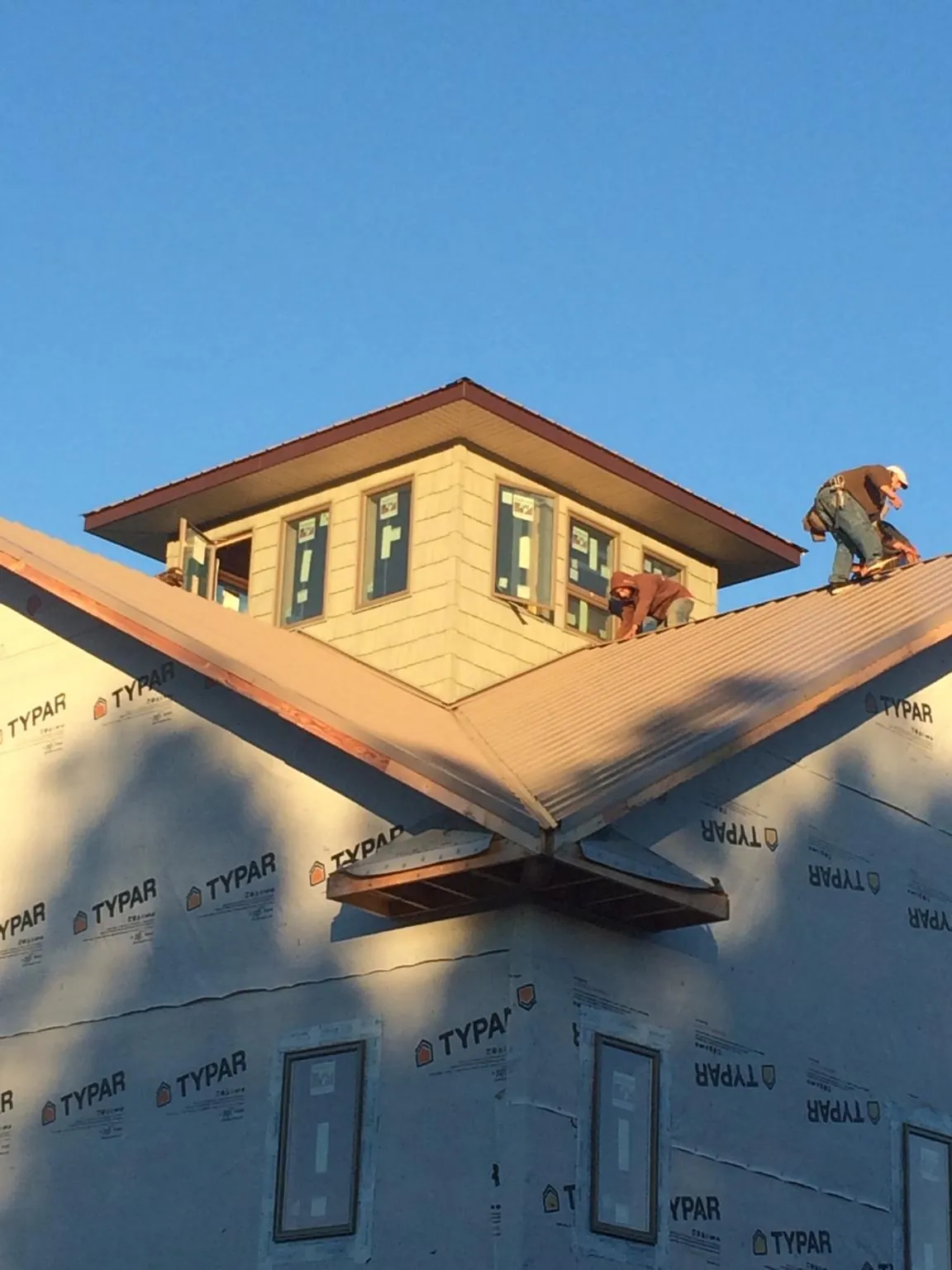 Roofers working around a rooftop cupola on a new metal roof at sunset — Roof Waterproofing in Washburn by Roofing Brothers